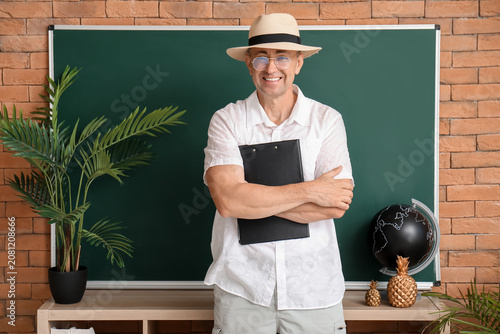 Male geography teacher with clipboard near blackboard in classroom