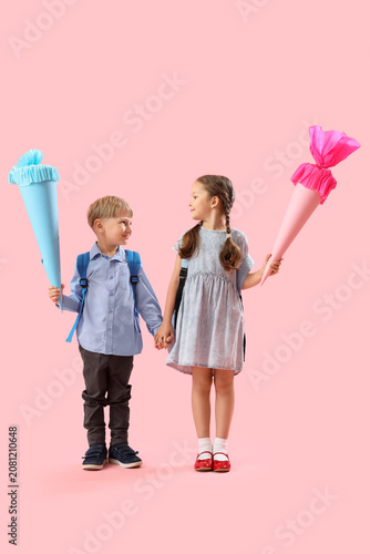 Happy little classmates with backpacks and colorful school cones on pink back...