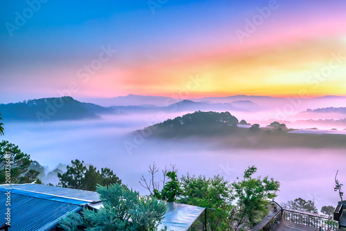 A breathtaking sunrise over a sea of clouds in the highlands, where soft layers of mist drift between rolling hills. The warm glow of the rising sun paints the sky in gentle orange and pink tones