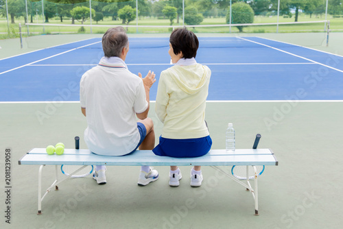 テニスコートのベンチで休憩するシニア夫婦の後ろ姿