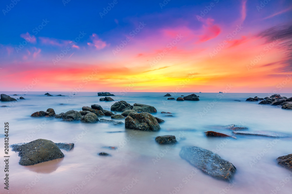 Naklejka premium Beautiful coastal sunrise scene featuring a dramatic rock formation rising from a sandy beach.