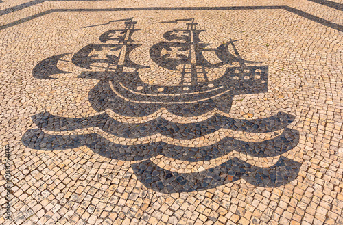 Traditional black and white stone pavement with a sailing ship mosaic in Lisbon, Portugal.