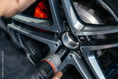 Fotografija Changing car wheel in auto repair shop using an electric drill to loosen the bolts