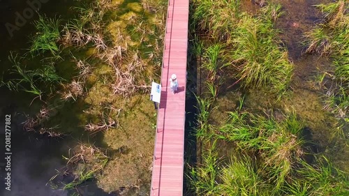 A girl walks across a bridge in the middle of a lake, filmed from a drone, viewed from above