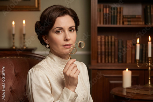 Woman with lorgnette glasses sitting in a vintage library at night  