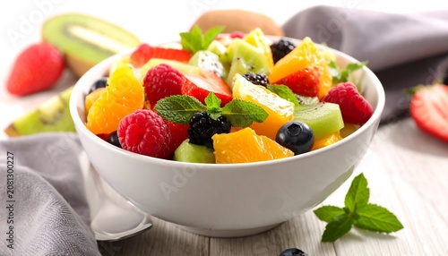 Close-up of a refreshing fruit salad in a white bowl, garnished with mint leaves on a wooden surface, with some fruit visible