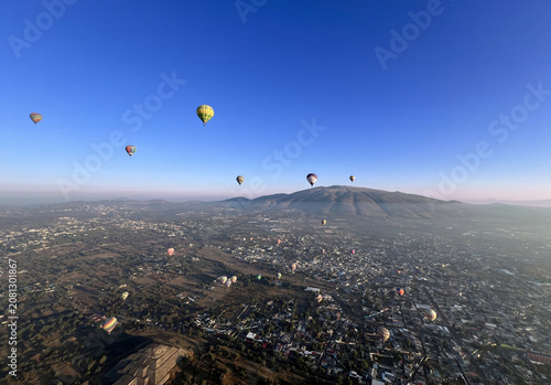 Aerial view of numerous hot air balloons drifting above the historic Pyramids of Teotihuacan with the sprawling town and distant mountains in Mexico City, Mexico City, Mexico.
