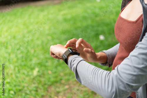 Asian Gen Z woman using smartwatch to track fitness activity during outdoor workout for wellness and healthy lifestyle.