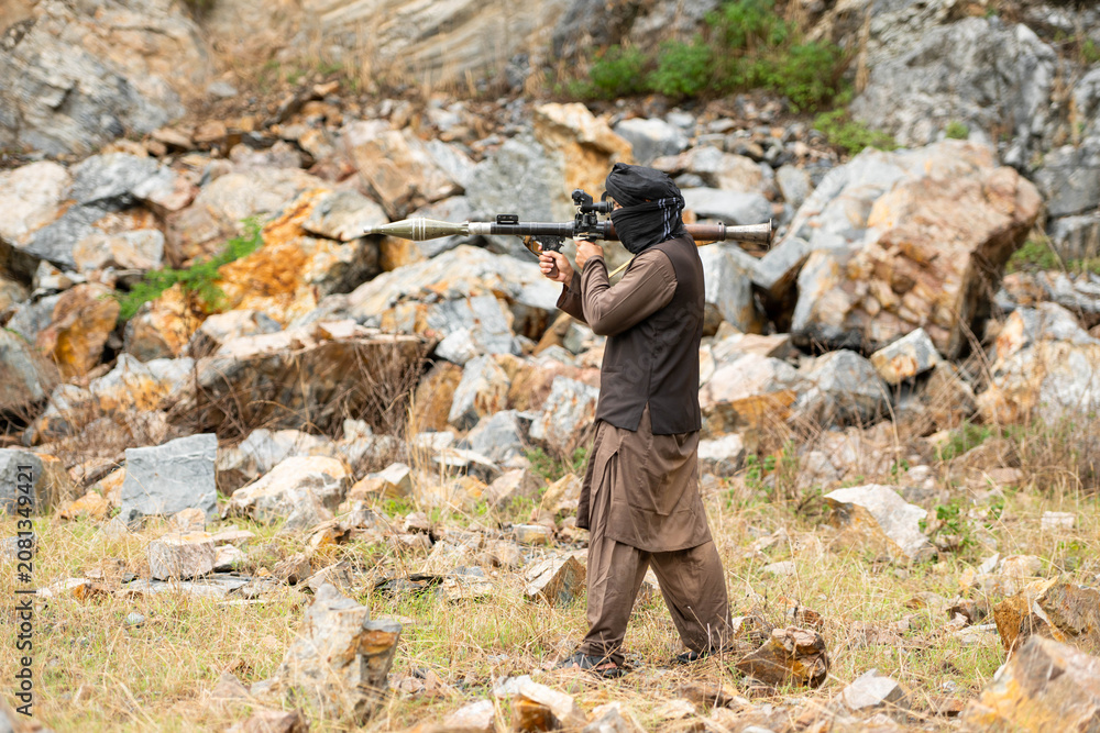 Fototapeta premium Armed militant aiming a rocket launcher during a simulated conflict scenario in rocky outdoor terrain