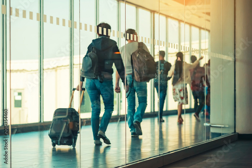 Photograph through large clear glass wall with blurred image of departing passengers and luggage walking airplane boarding corridor from terminal to plane in background. Selective focus on glass.