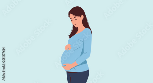 Beautiful pregnant woman with long hair wearing a blue shirt and holding her belly while looking down with a gentle smile.
