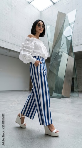 Stylish woman in striped pants walking in modern gallery