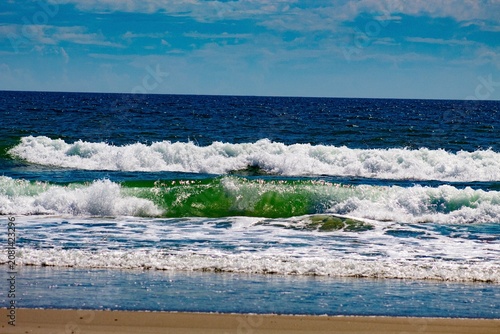 Powerful ocean waves breaking on a sandy beach under blue sky, coastal seascape, surf and sea foam, natural shoreline landscape, summer travel and nature background