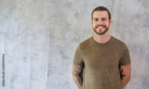 Foto Portrait of bearded caucasian man with tattoos standing against a textured gray background, expressing confidence, friendliness, and a casual modern lifestyle
