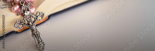 A silver crucifix with elegant, ornate details and a string of pink beads rests on an open book, symbolizing a moment of quiet reflection and religious study.