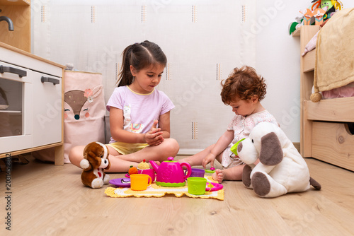 Quadro su tela A 5-year-old girl and her 14-month-old baby sister having a pretend picnic with stuffed animals in their bedroom