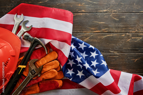 American flag with construction tools, safety helmet, hammer, wrench and work gloves on rustic wooden table with copy space, patriotic labor and construction industry concept for Labor Day, skilled