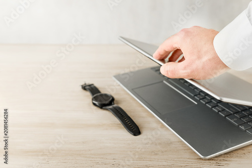 Hand using laptop near smartwatch on light wooden desk with copy space, modern technology and business workspace concept for digital trust, data privacy, cybersecurity, secure access, online identity