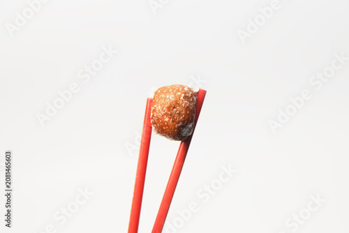 Fotografía A single rotten strawberry covered in white, fuzzy mold, held up vertically by a pair of red chopsticks against a clean, plain white background