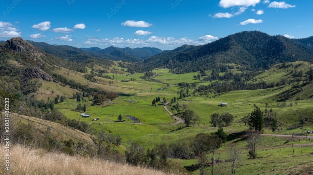 Obraz premium Expansive Green Valley Landscape Surrounded by Rolling Hills and Blue Sky with Fluffy Clouds Under Bright Sunlight