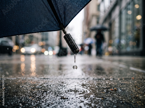Rainy day city street view from under dark umbrella puddle
