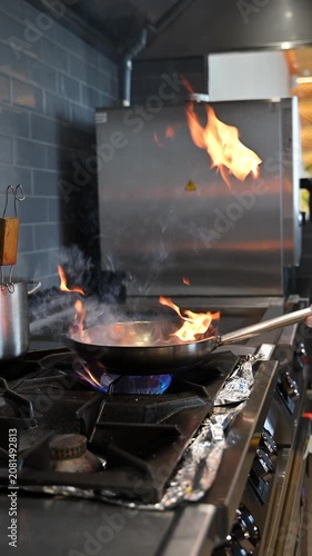 Fire flare in a pan as a professional chef cooks on a commercial gas stove range in a restaurant kitchen. Cinematic b roll for food and beverage content. Slow motion video 