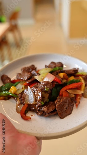 Waiter's hand reaching up to carry a freshly prepared plate of beef stir-fry from the kitchen pass to a restaurant dining table. Waiter carrying a dish from the kitchen to the table. Cinematic b roll.