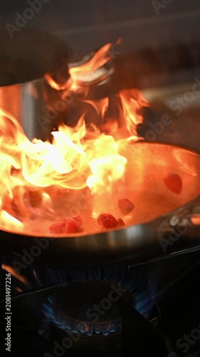 Closeup of a pan with frying ingredients in flames. Cook flipping ingredients in a pan with fire flare on a gas stove in a restaurant kitchen. Beautiful flames in a pan on a new modern kitchen.