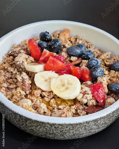 Close-up of a delicious granola breakfast bowl topped with sliced bananas, fresh berries, and a drizzle of golden honey
