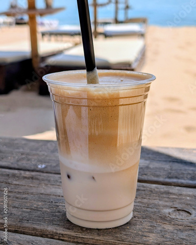 Close-up of a refreshing Greek frappe coffee with thick foam in a glass on a sandy beach with the blue ocean background