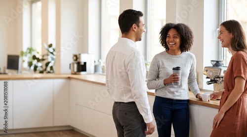 Diverse colleagues chatting and drinking coffee in modern office kitchen
