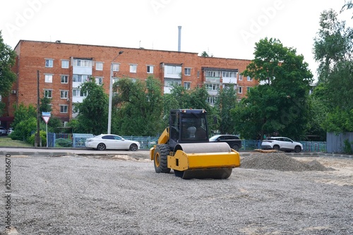 Obraz na plátně Road roller machine is compacting gravel on a construction site with residential buildings in the background