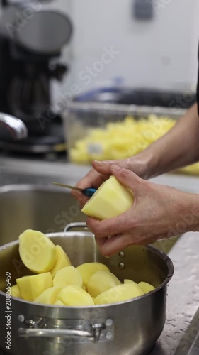 Hands peeling a raw potato with a knife over a pot of peeled potatoes