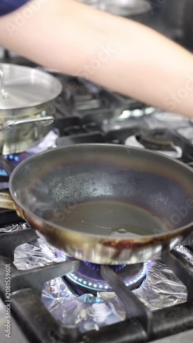 Chicken pieces cooking in a frying pan over a blue gas flame on the stove
