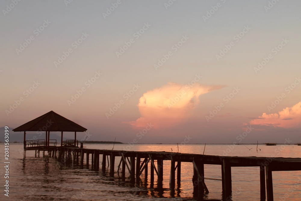 Obraz premium Wooden pier with a gazebo at sunset in Tanjung Lesung Beach, Banten, Indonesia. Eye-level view with natural focus captures a peaceful coastal mood, perfect for travel, tourism, relaxation, and nature