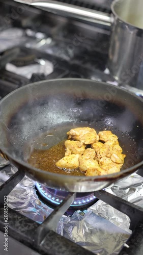 Chicken pieces cooking in a frying pan over a blue gas flame on the stove