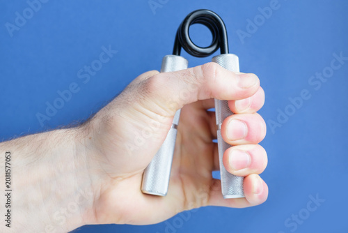 A man's hand squeezes and unclenched an expander to strengthen his grip on a blue background, close-up.