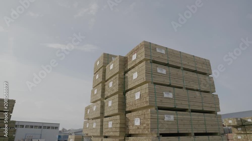 Large stacks of bundled wood planks stored in an open-air lumber yard under a cloudy sky, ready for transport, distribution, or construction use