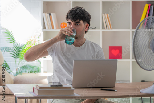 Young man at home drinking at his desk with a laptop