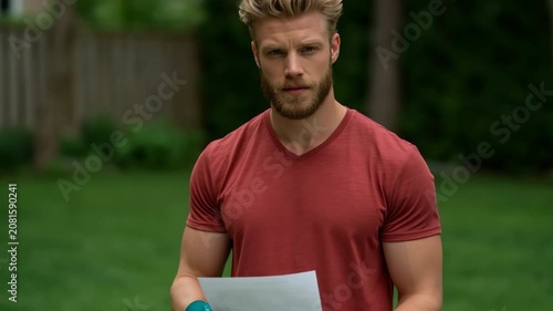 Adult man holding paper outside on residential lawn