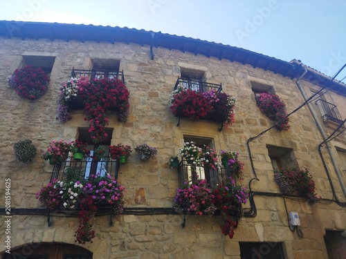 Fachada tradicional de piedra con balcones repletos de geranios de colores en Hoyos, Sierra de Gata, Cáceres, España.