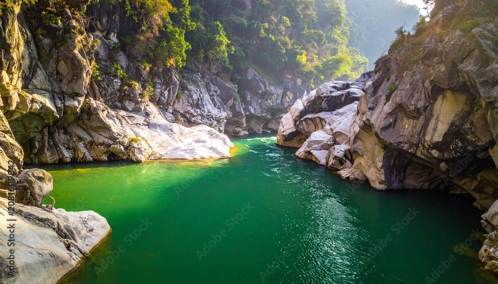 Obraz premium Serene emerald river winding through rocky canyon with lush forest.