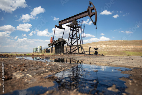 Oil Pumpjack with Crude Oil Reflection in Foreground Under Blue Sky – Petroleum Extraction and Energy Industry in Rural Landscape