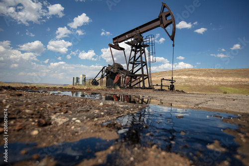 Oil Pumpjack with Crude Oil Reflection in Foreground Under Blue Sky – Petroleum Extraction and Energy Industry in Rural Landscape