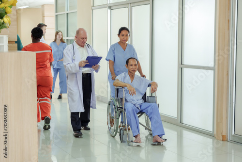 Konstfotografi Senior asian male patient in wheelchair accompanied by female nurse and caucasia