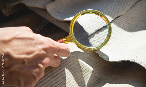 Male hand with a magnifying glass showing old asbestos roof. Health problems