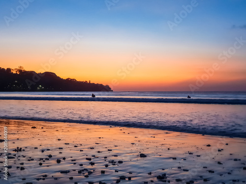 Foto Jimbaran Beach shoreline at twilight with orange afterglow sky and silhouetted h