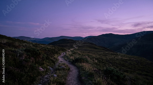 A winding path through rolling hills under a twilight sky, bathed in soft purple and blue hues, evoking a sense of journey and tranquility