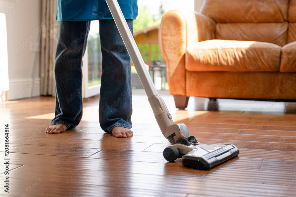 Fototapeta premium Person cleans wooden floor using vacuum in living room during daytime with sunlight coming through windows