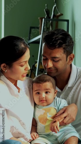 Indian parents and baby boy sitting near bedroom window on cozy bed, mother lovingly points outside, capturing emotional family bonding, modern parenthood, parenting lifestyle, newborn care at home